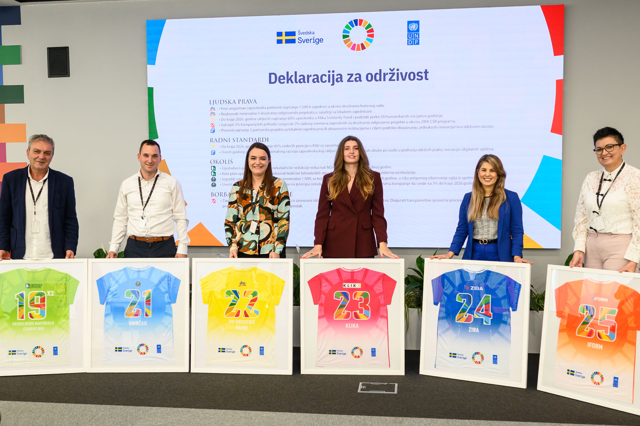 Zaposlenici poziraju s plakatima tokom korporativnog događaja o održivosti.