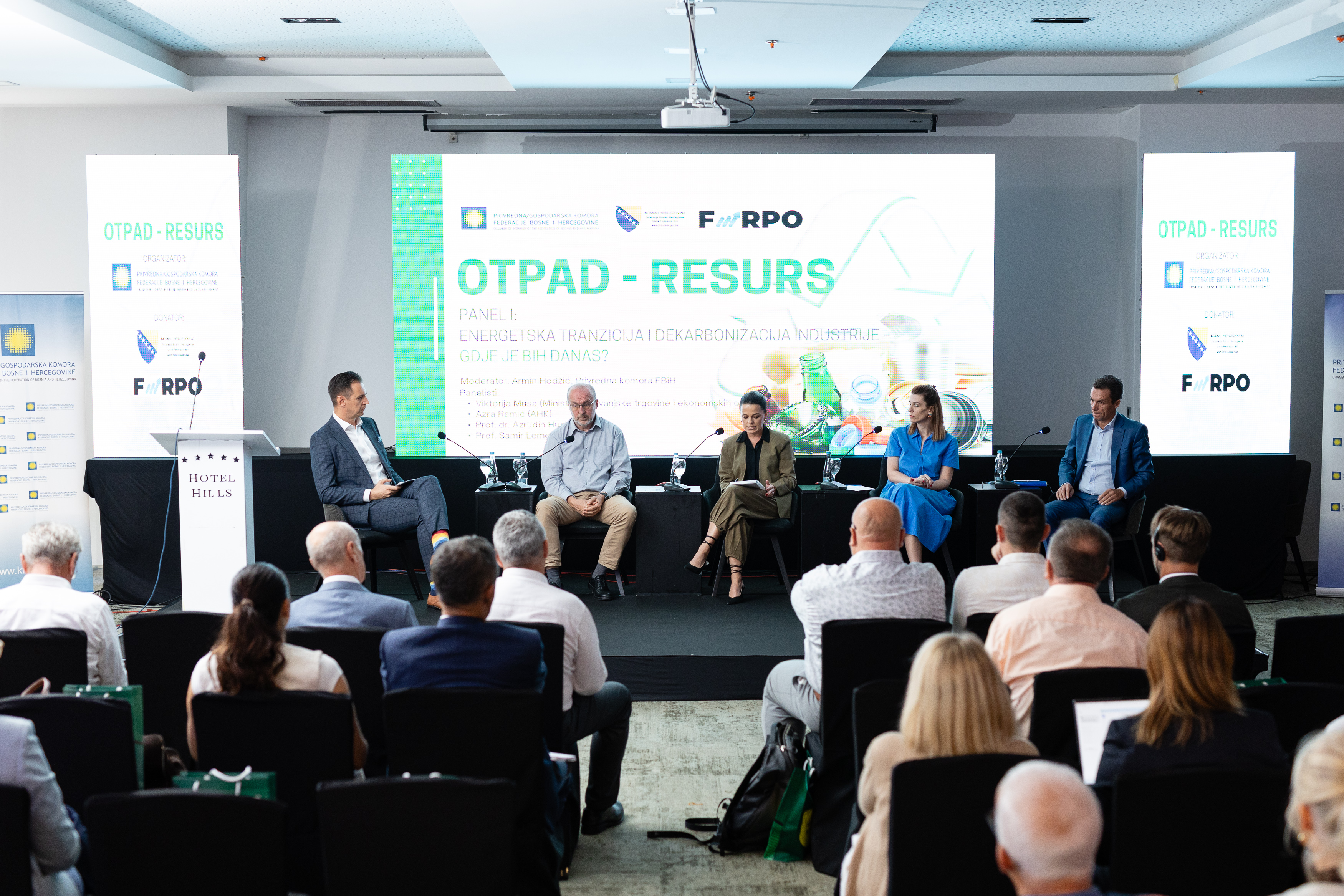 Panel diskusija s pet osoba na bini i publikom u konferencijskoj sali, tema otpada kao resursa prikazana na ekranu u pozadini.