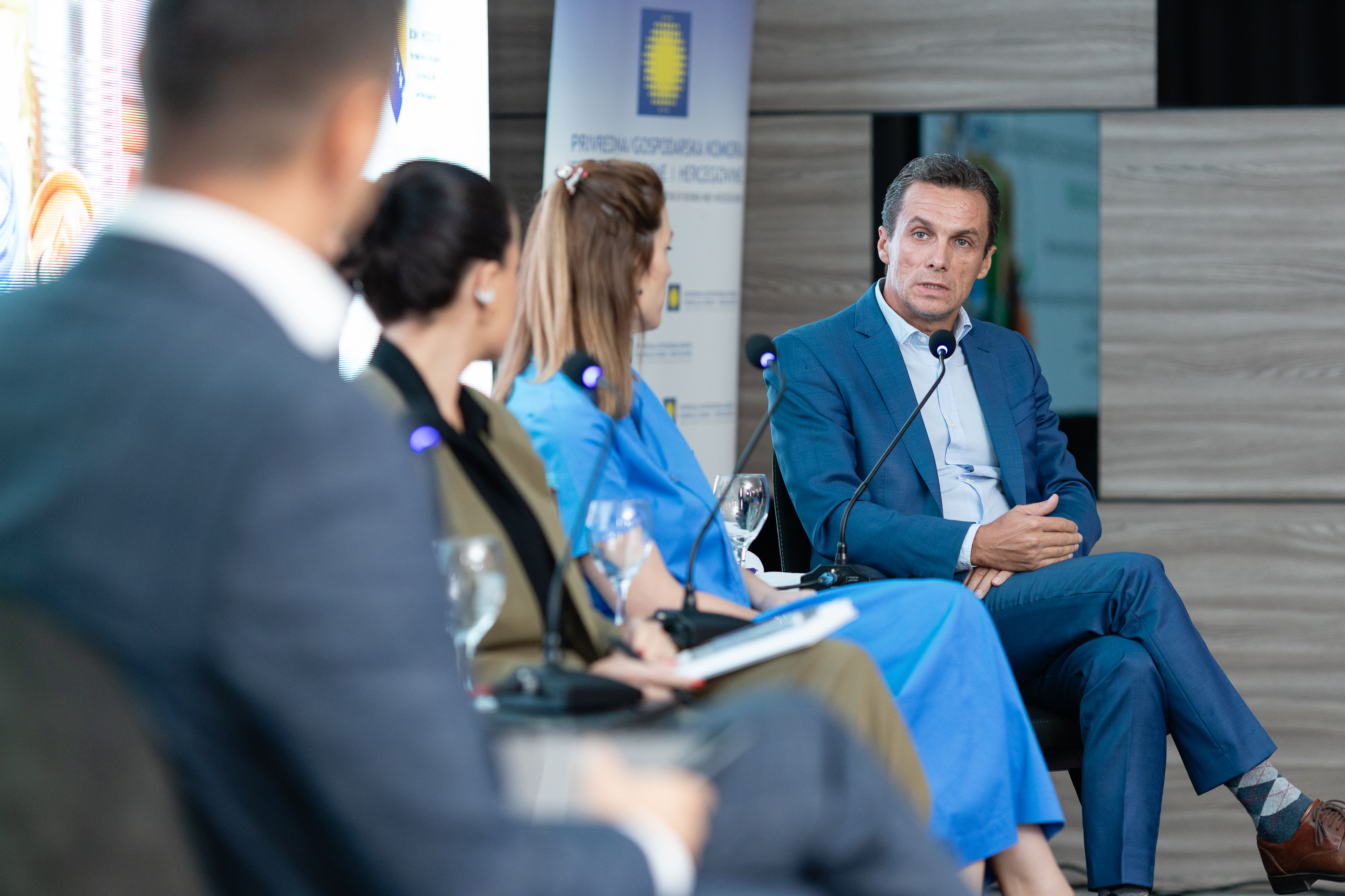 Ljudi sjede i panel diskusiji, jedan muškarac u plavom odijelu aktivno govori.