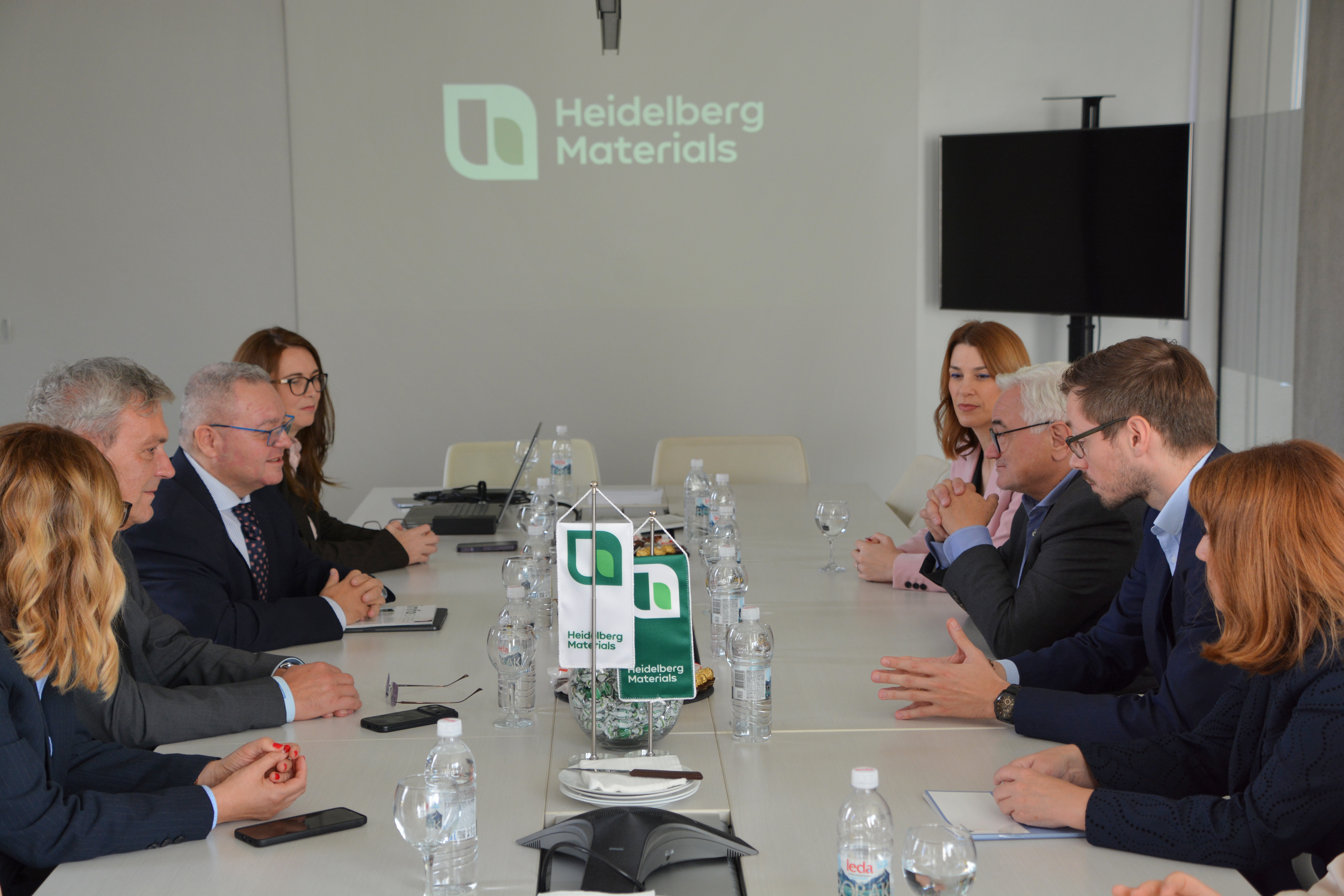 Sastanak poslovnog tima za stolom u prostoriji sa logotipom Heidelberg Materials na zidu.